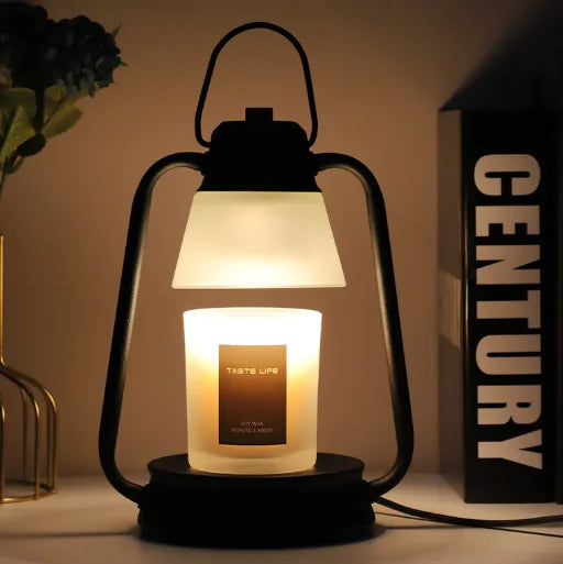 Decorative lantern with a lit candle inside, placed on a surface with a book and plant in the background.