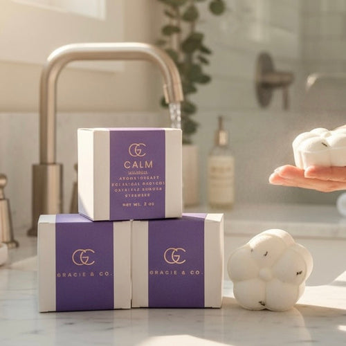 Two boxes of Gracie & Co. Calm soap on a bathroom counter with a hand holding a bar of soap.
