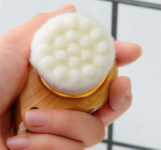 Hand holding a wooden facial cleansing brush with a white bristle head.