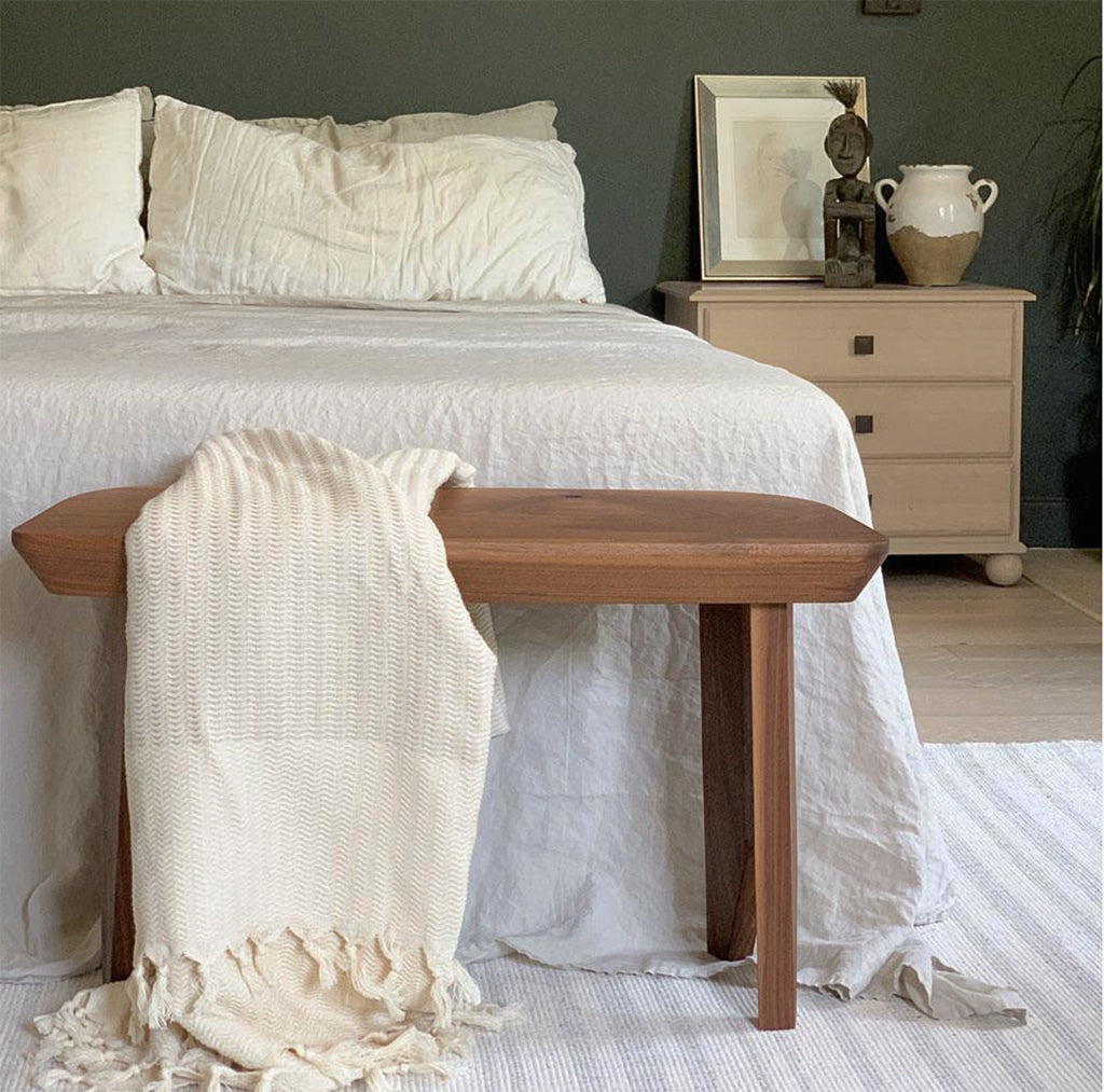 Wooden bench with a blanket in front of a bed in a bedroom setting.