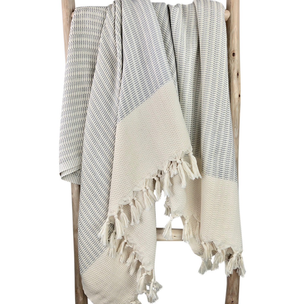 Textured throw blanket with tassels draped over a wooden ladder on a white background